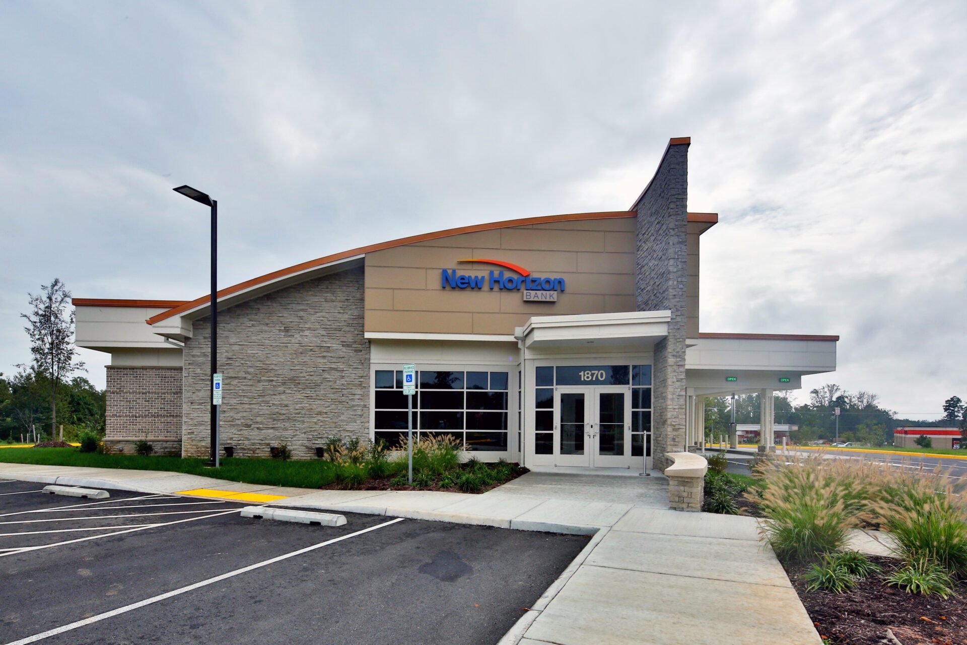 Exterior of New Horizon Bank building with clear signage, parking lot in the foreground, and overcast sky